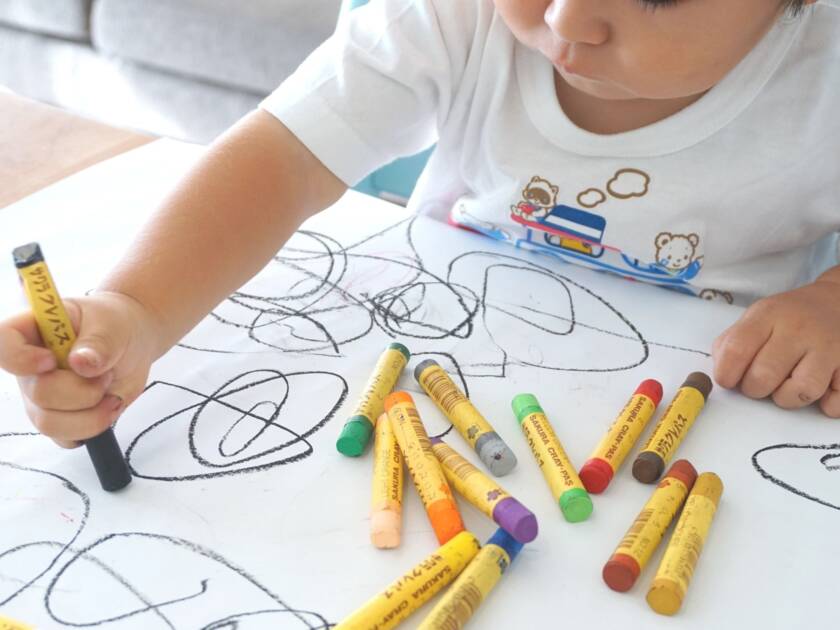 A child is drawing with crayons on a white paper.