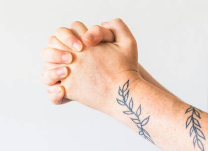 Hands held together in prayer. There is a tattoo of blue leaves on the arm.