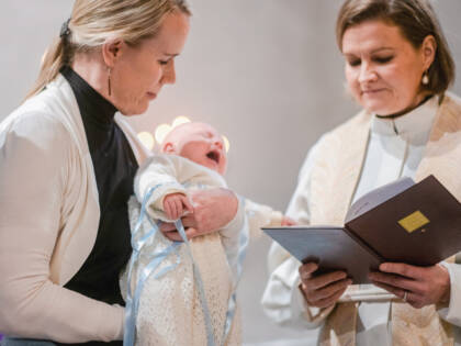 A pastor stands next to a woman holding a baby.