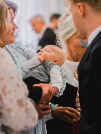 A baby is in the woman's arms, where the christening guests can admire him.