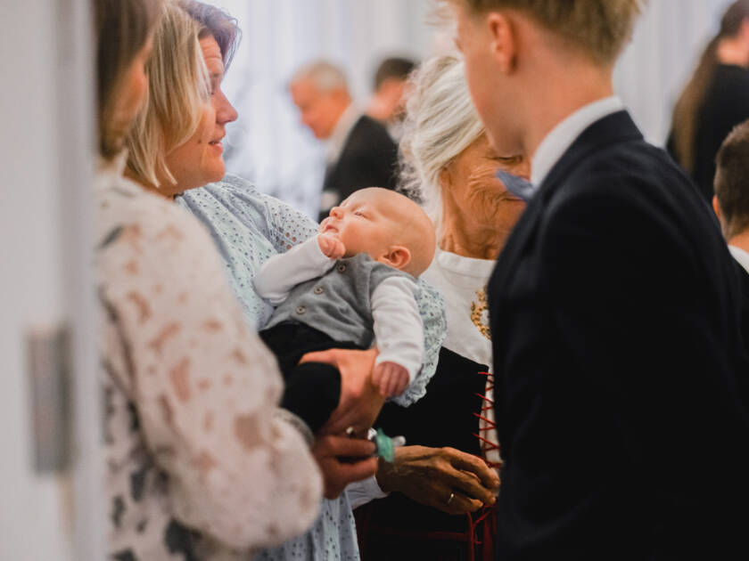 A baby is in the woman's arms, where the christening guests can admire him.