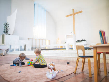 Kaksi lasta leikkii kirkon lattialla aurinkoisena päivänä.