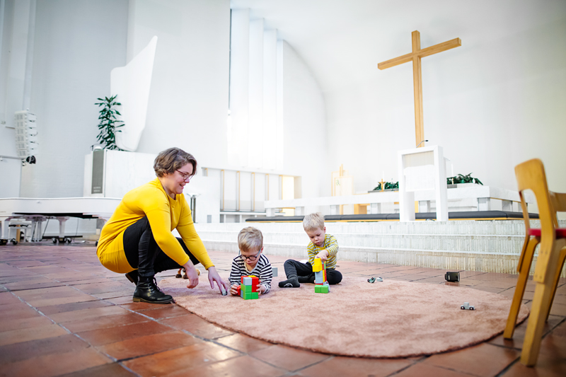 Nainen leikkii lasten kanssa kirkossa alttarin edessä.