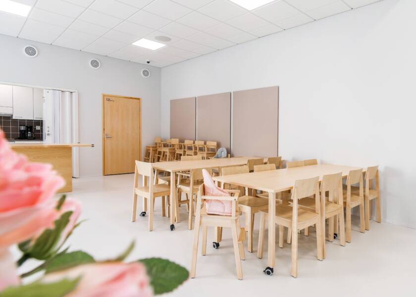 A light-coloured room with light-coloured wooden furniture. A flower in the foreground.