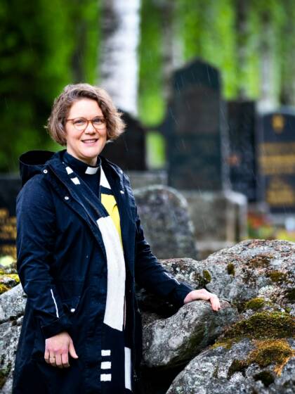 Naispapi nojaa kivimuuriin hautausmaalla. Taustalla hautakiviä.