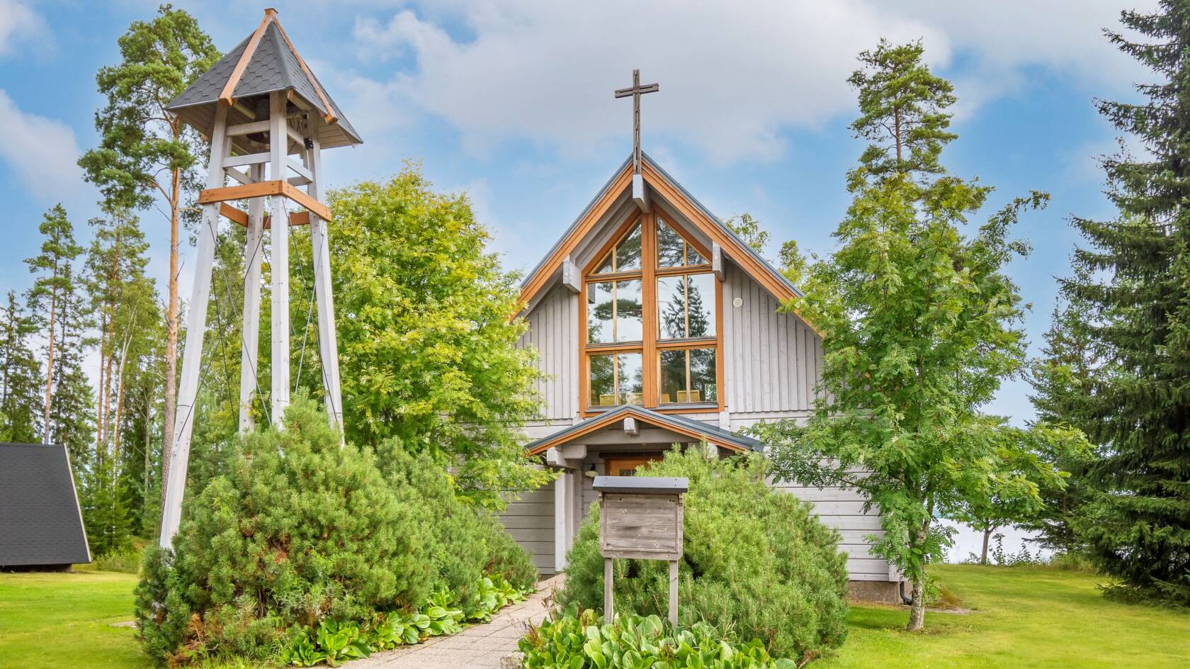 Pieni puinen, vaalea kirkko puiden ja pensaiden keskellä.