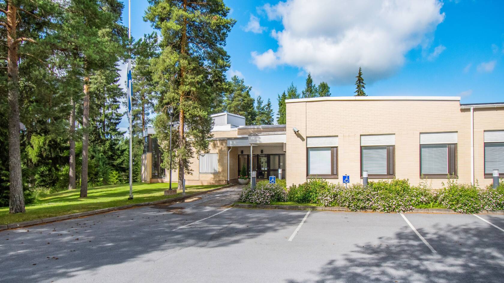 Keltatiilinen rakennus ruskeilla ikkunakarmeilla. Puita rakennuksen ympärillä.