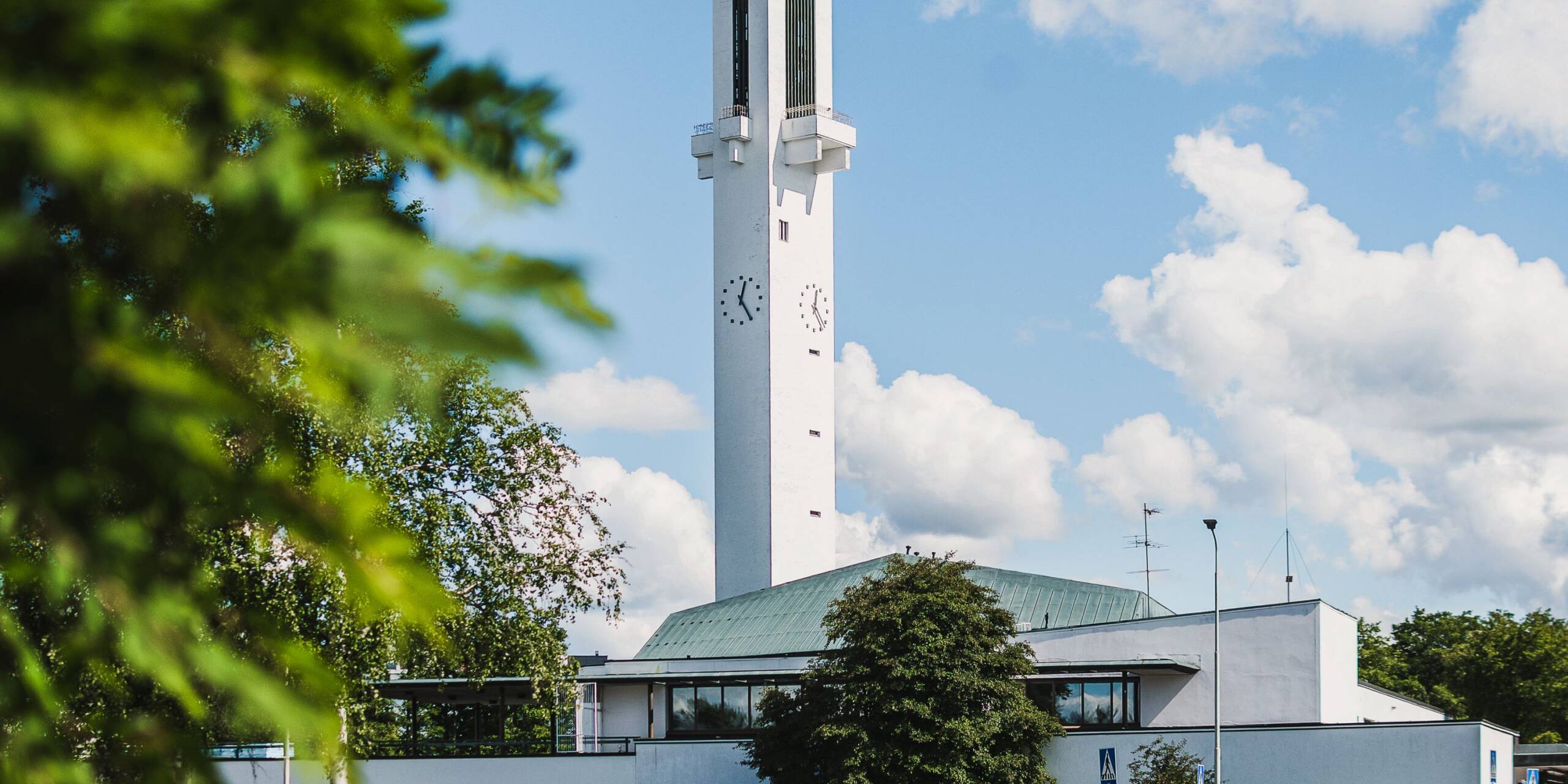 Valkoinen kirkko, jossa korkea ristinmallinen torni ja kello.