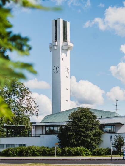 Valkoinen kirkko, jossa korkea ristinmallinen torni ja kello.