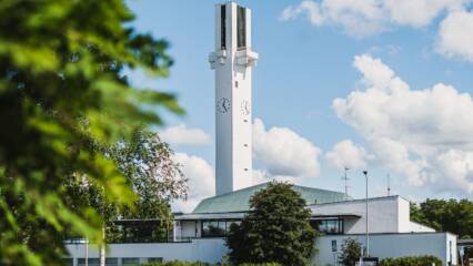 Valkoinen kirkko, jossa korkea ristinmallinen torni ja kello.