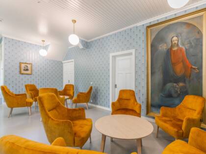 Aula, jossa on sinapinkeltaisia nojatuoleja ja pyöreät puunväriset sohvapöydät. Seinillä sinikuvioinen tapetti ja iso taulu. Valkoiset ovet ja pyöreät lamput.