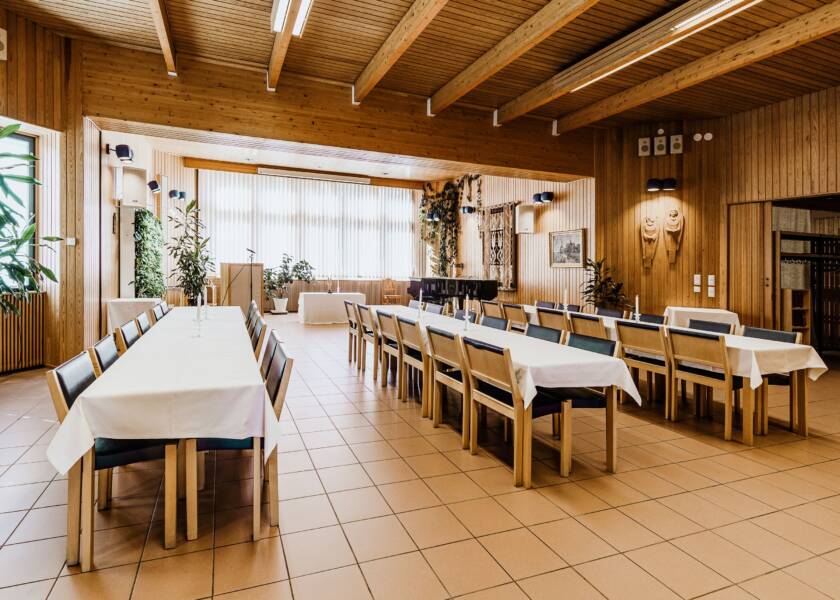 Tila, jossa laattalaattia ja paljon puuta. Pitkät pöydät ja tummalla verhoillut puiset penkit.