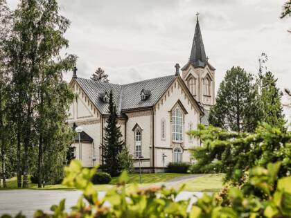 Vaalea kirkko koristeellisilla yksityiskohdilla. Puita ympärillä.