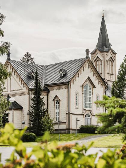 Vaalea kirkko koristeellisilla yksityiskohdilla. Puita ympärillä.