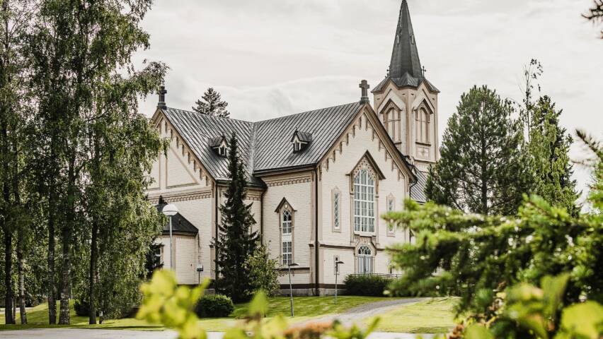 Vaalea kirkko koristeellisilla yksityiskohdilla. Puita ympärillä.