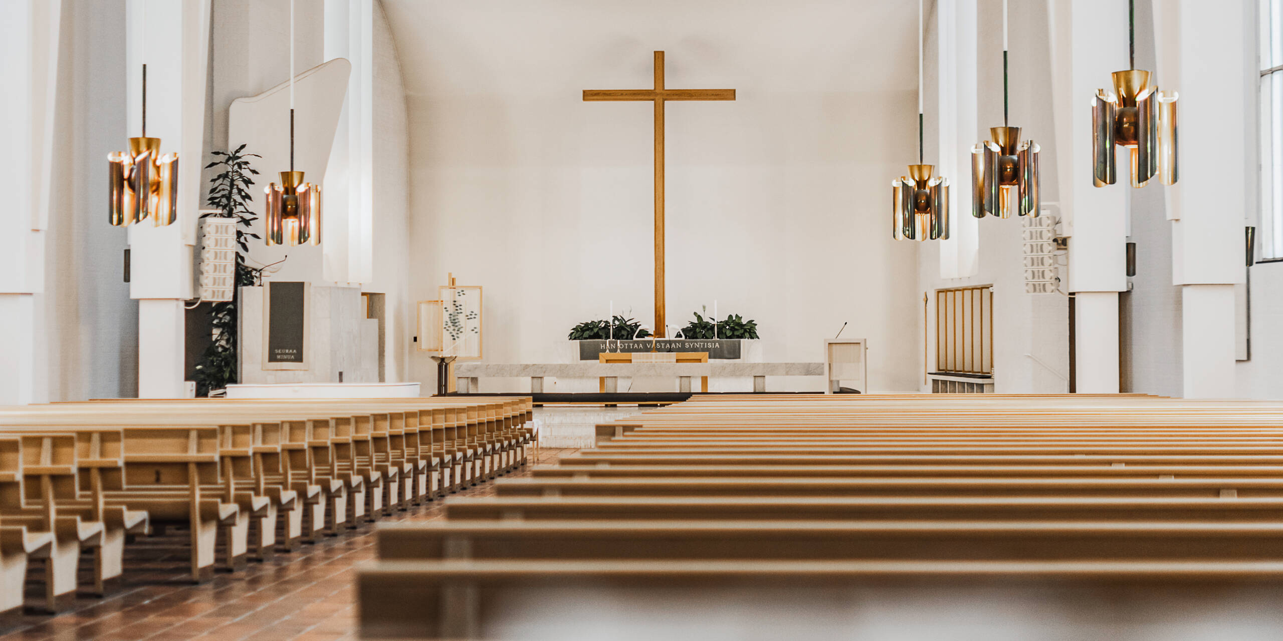 Kirkkotila, jossa näkyy puusta tehtyjä kirkonpenkkejä, alttari ja risti.