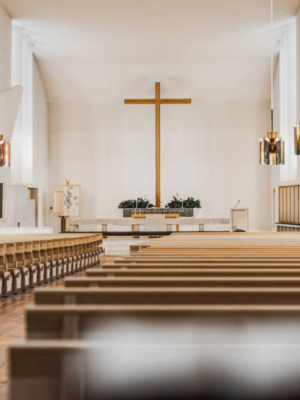 Kirkkotila, jossa näkyy puusta tehtyjä kirkonpenkkejä, alttari ja risti.