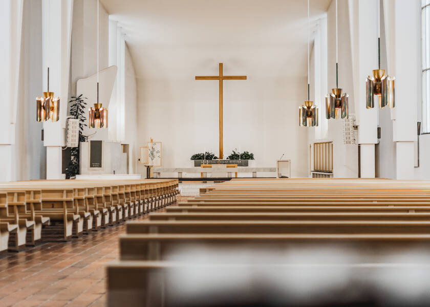 Kirkkotila, jossa näkyy puusta tehtyjä kirkonpenkkejä, alttari ja risti.