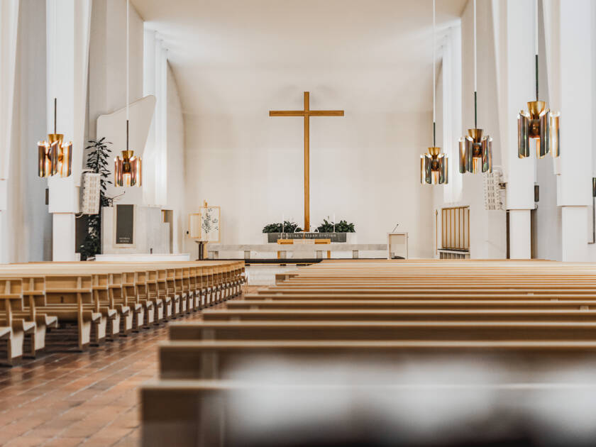 Kirkkotila, jossa näkyy puusta tehtyjä kirkonpenkkejä, alttari ja risti.