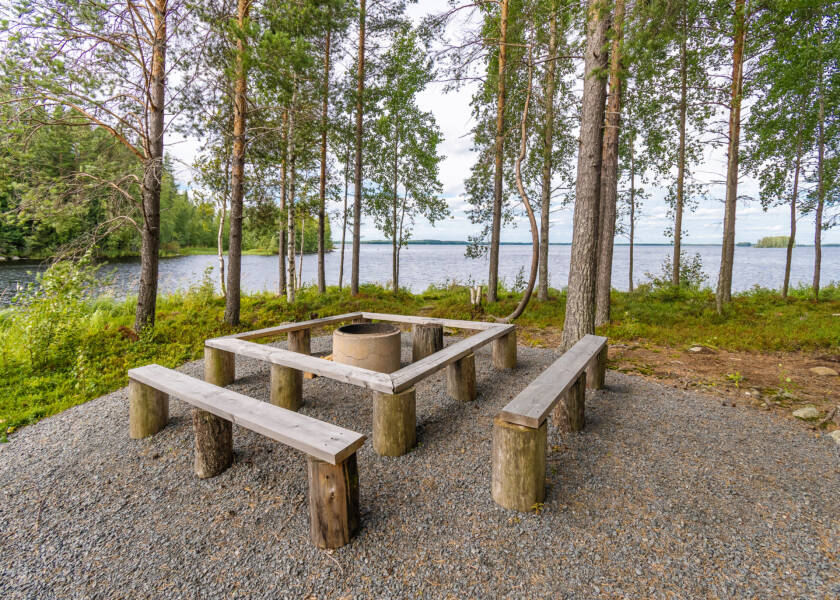 Nuotiopaikka jonka ympärillä pitkät penkit. Taustalla järvi.