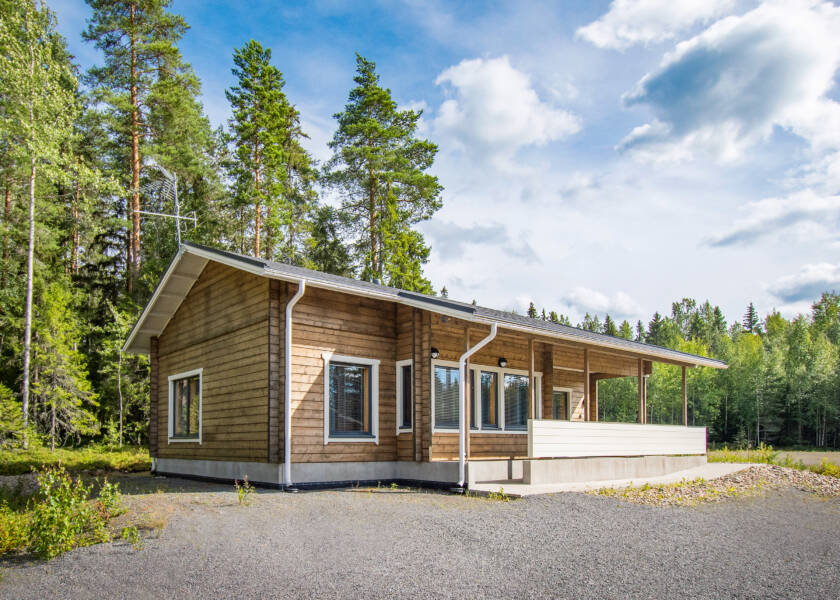 Hirsinen ruskea matala rakennus, ympärillä kuusia.