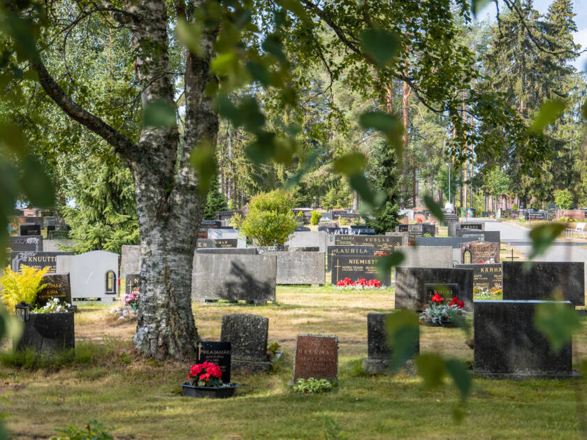 In the cemetery, there are gravestones, flowers, and trees.