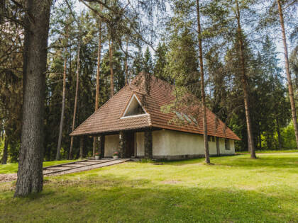 Pieni punatiilikattoinen kirkko korkeiden kuusien ja mäntyjen keskellä. Ympärillä nurmikkoa.