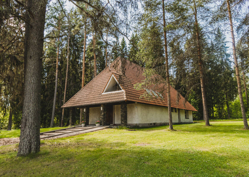 Pieni punatiilikattoinen kirkko korkeiden kuusien ja mäntyjen keskellä. Ympärillä nurmikkoa.