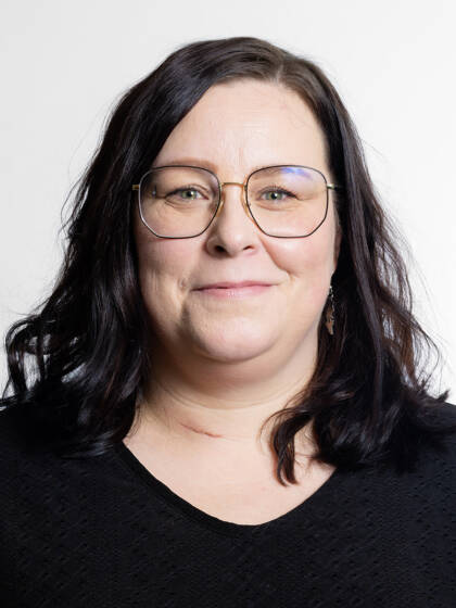 Kasvokuva henkilöstä jolla on tumma olkapäille ulottuva tukka ja silmälasit.