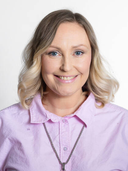 Close-up portrait of a person with shoulder-length wavy blonde hair, bangs, and a light pink collared shirt.