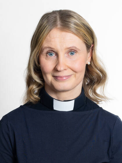 Kasvokuva henkilöstä jolla on olkapäille ulottuva vaalea tukka ja papinkaulus.