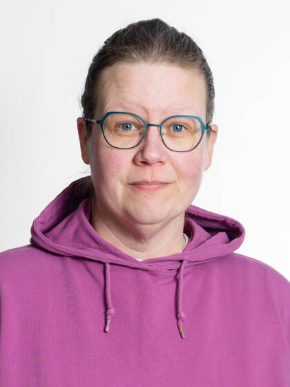Kasvokuva henkilöstä jolla on hiukset kiinni takana, silmälasit ja violetti huppari.