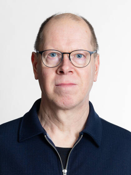 Kasvokuva henkilöstä jolla on siili tukka ja silmälasit.