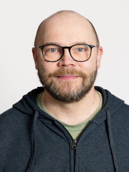 Henkilö jolla on siili tukka, silmälasit, viikset ja partaa.