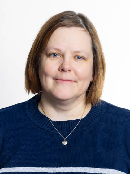 Kasvokuva henkilöstä jolla on polkkatukka, hopeinen kaulakoru ja tummansininen neulepaita.