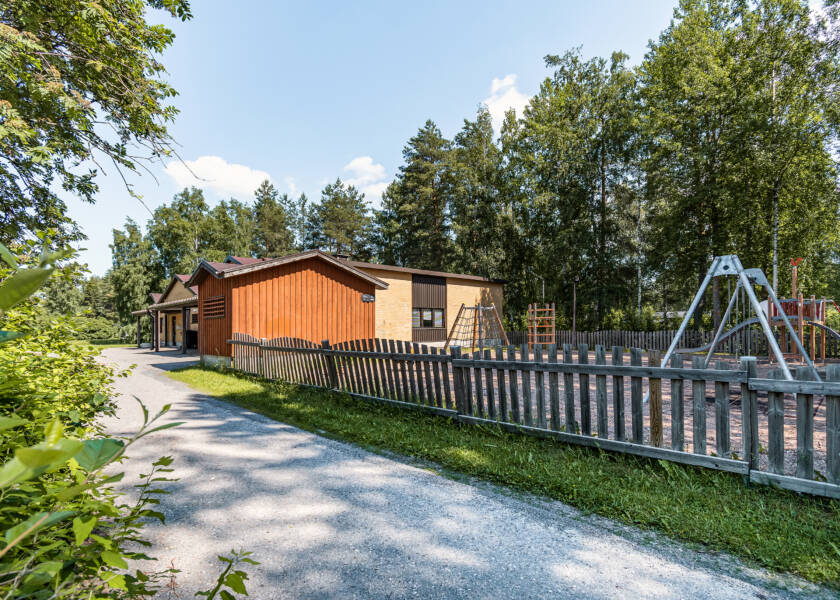 Aita jonka takana leikkipuisto ja keltatiilinen rakennus.