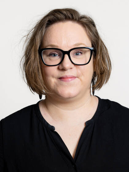 Kasvokuva henkilöstä jolla on ruskea polkkatukka sekä mustat paksusankaiset silmälasit.