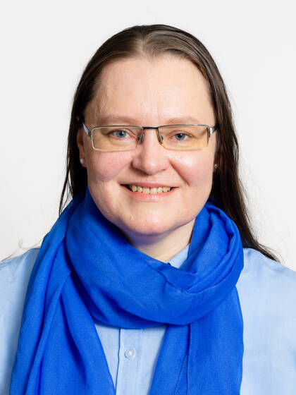 Kasvokuva henkilöstä jolla on pitkä tumma tukka ja silmälasit sekä sininen kaulahuivi.