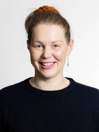 Kasvokuva henkilöstä jolla on hiukset kiinni oranssilla donitsilla sekä korvakorut ja musta paita.