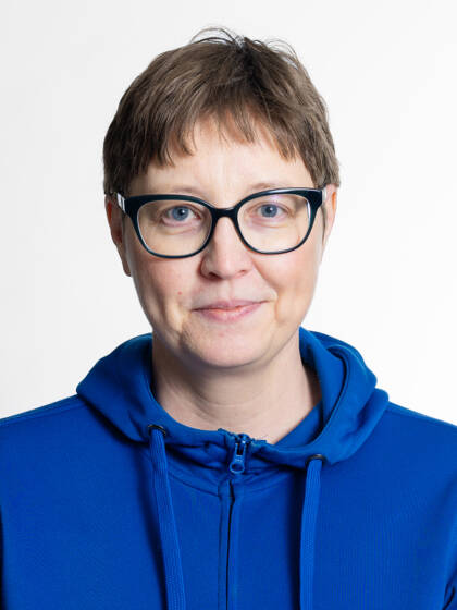 Kasvokuva henkilöstä jolla on lyhyet ruskeat hiukset ja silmälasit ja sininen paita.