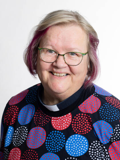 Kasvokuva henkilöstä jolla on on vaaleat hiukset jossa punaista raitaa, silmälasit sekä papinkaulus.