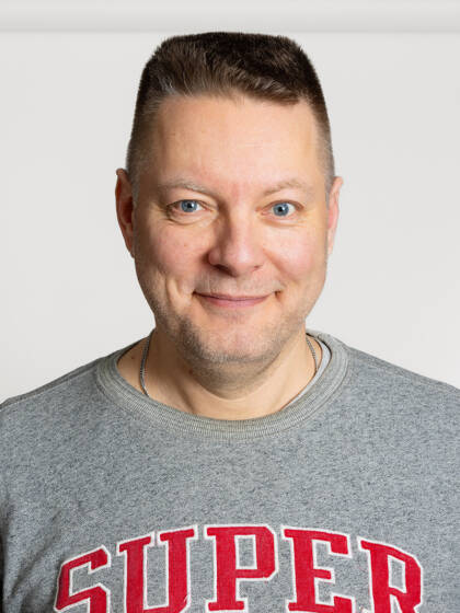 Henkilö jolla on lyhyet hiukset ja harmaa paita jossa punainen teksti.