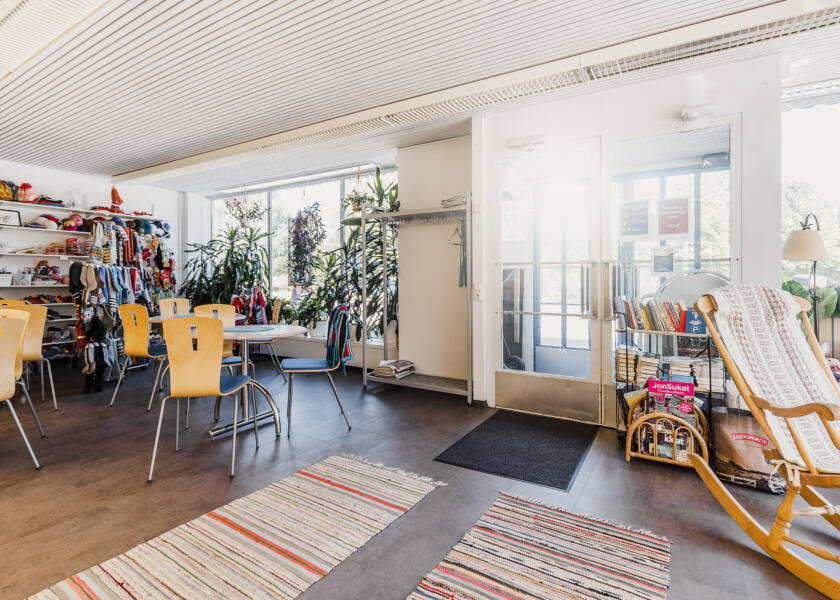 Tila jossa keinutuoli ja pari pöytäryhmää. Ikkunan vieressä viherkasveja ja teline jossa myytäviä villasukkia.