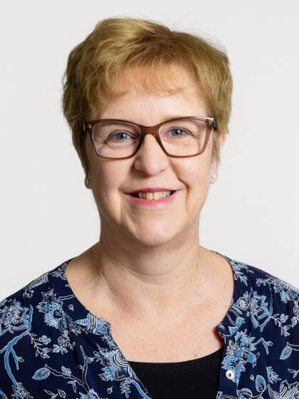 Henkilö jolla on vaaleat lyhyet hiukset, silmälasit ja helmikorvakorut.