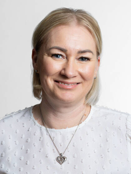Henkilö jolla on vaalea polkka osittain takana kiinni, valkoinen paita ja hopeinen sydänkaulakoru.