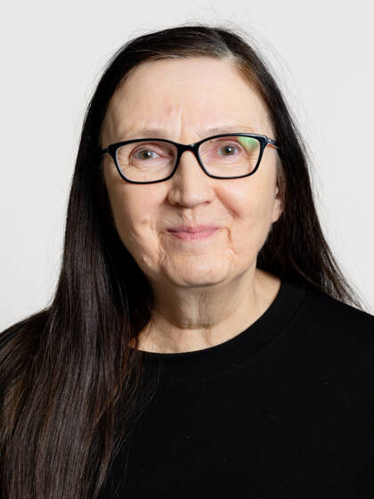 Henkilö jolla on musta pitkä tukka, silmälasit sekä musta paita.