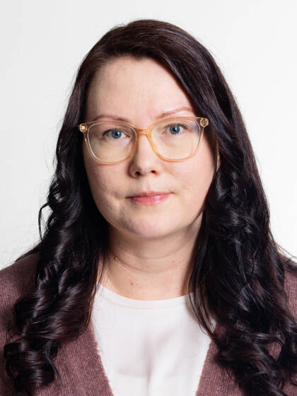 Henkilö jolla on pitkät laineikkaat tummat hiukset ja silmälasit.