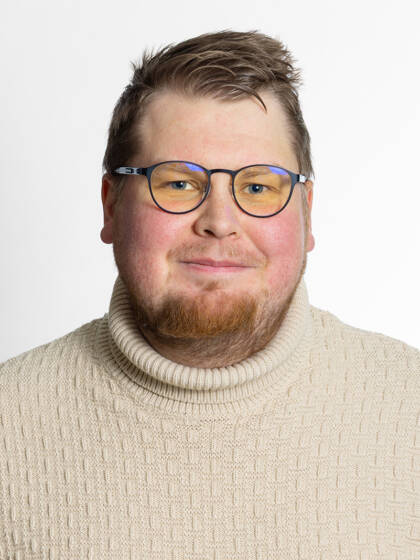 Kasvokuva henkilöstä jolla on silmälasit, lyhyet hiukset, lyhyttä partaa ja vaalea villaneule.