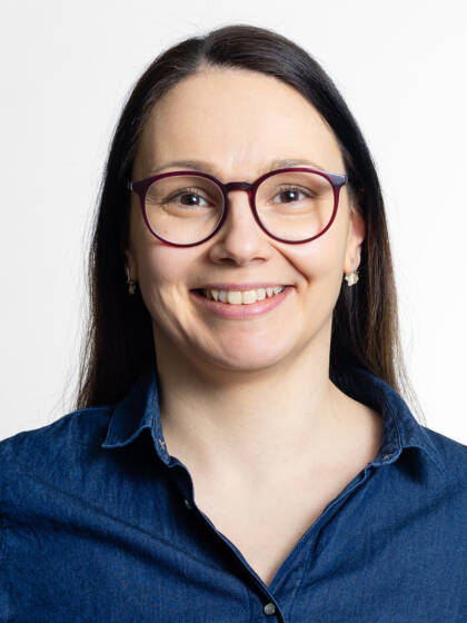 Henkilö jolla on pitkät tummat hiukset ja silmälasit. Korvissa hopeanväriset korvakorut.