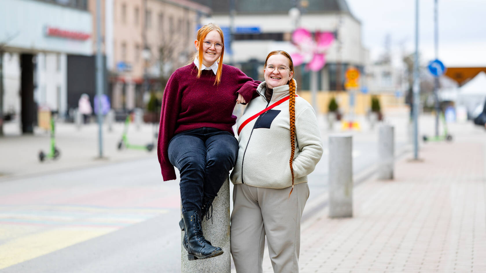 Kaksi punahiuksista henkilöä taustallaan kaupunkia.